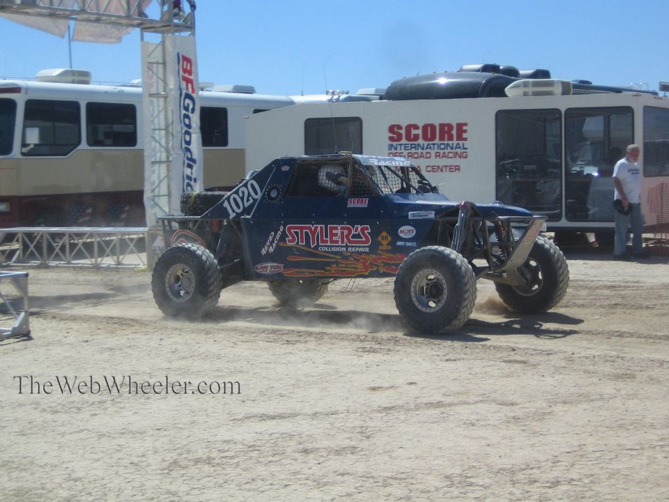 Blue number 1020 Stylers off-road buggy on dirt past SCORE media center