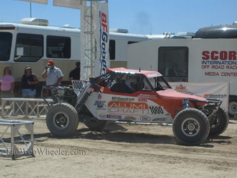 1990 Ford Bronco - red and white Alumi Craft off-road buggy numbered 1000 stages by a BFGoodrich gate as spectators watch.