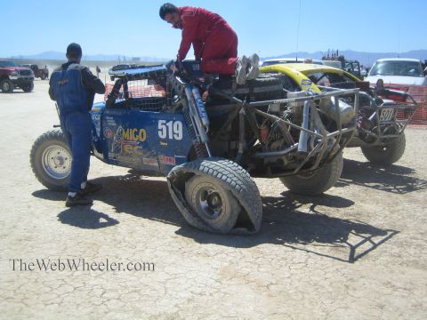 1990 Ford Bronco - Crew members tend to a blue off-road race car numbered 519 in a cracked-mud desert pit, one climbing on the cage.