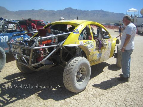 1990 Ford Bronco - Rear three-quarter view of a yellow Baja Bug numbered 501 with exposed engine as a man inspects it in the desert.