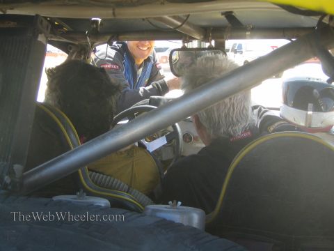 1990 Ford Bronco - Looking through a race car's roll cage, a smiling crew member in a Pyrotech suit leans toward two occupants.