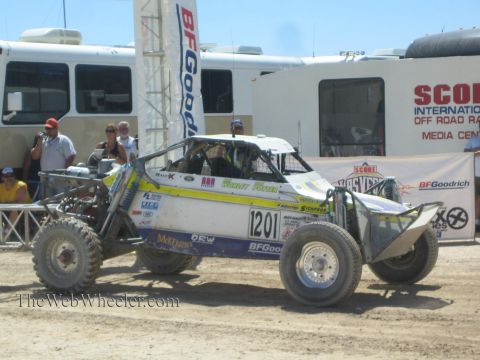 1990 Ford Bronco - white and yellow tube-frame off-road buggy numbered 1201 sits before BFGoodrich and SCORE Off Road Racing media-center banners.