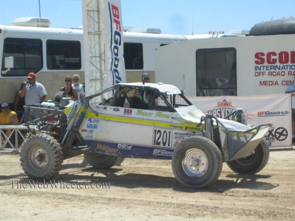 White and yellow off-road race buggy number 1201 in front of BFGoodrich and SCORE banners