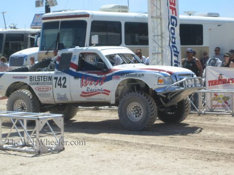 1990 Ford Bronco - white, red and blue Werz Racing off-road truck numbered 742 sits in a staging area as spectators watch nearby.