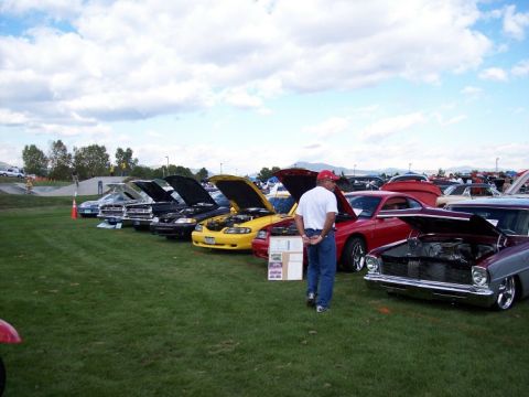 1972 Ford Ranchero - A car show features several vehicles with their hoods open on a grassy field under a cloudy sky.