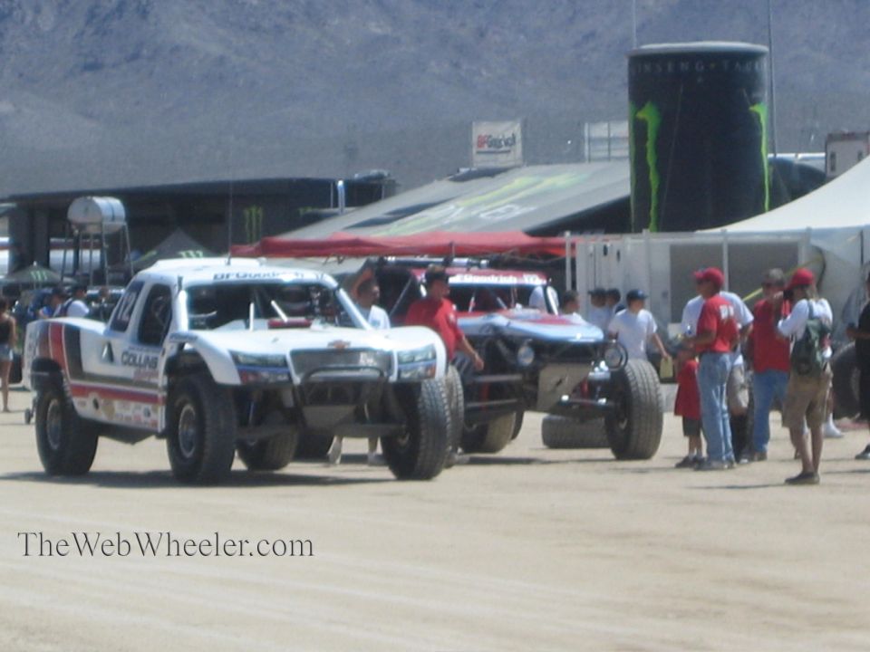 White off-road race trucks driving past Monster Energy displays and spectators
