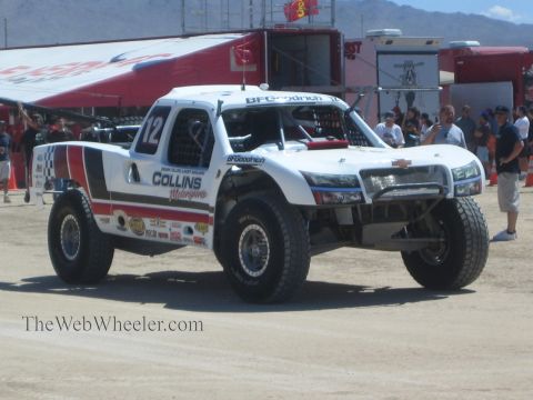 1990 Ford Bronco - white Collins Motorsports off-road race truck numbered 12 in BFGoodrich livery sits in a staging area with spectators nearby.