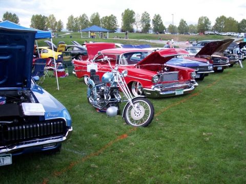 1972 Ford Ranchero - A custom motorcycle and several classic cars are displayed on a grassy field at an outdoor car show.