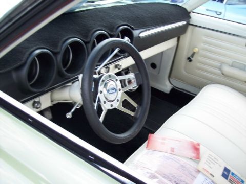 1972 Ford Ranchero - The interior of a car shows a steering wheel, dashboard, and white seats with some papers on them.