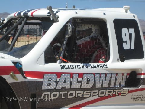 1990 Ford Bronco - Close-up of a white Baldwin Motorsports off-road race truck numbered 97, showing a helmeted driver inside the caged cab.