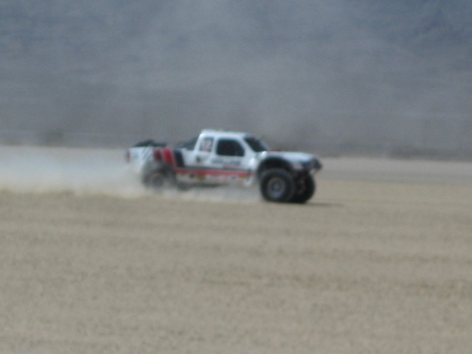 White off-road race truck speeding across desert dry lakebed kicking up dust