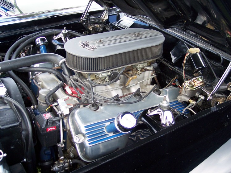 Ford V8 engine bay, showing dual carburetors, chrome valve covers with blue inserts, and an oval air cleaner