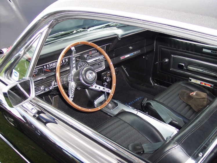 Car interior with wood steering wheel, black seats, and dashboard. A brown hat rests on the passenger seat