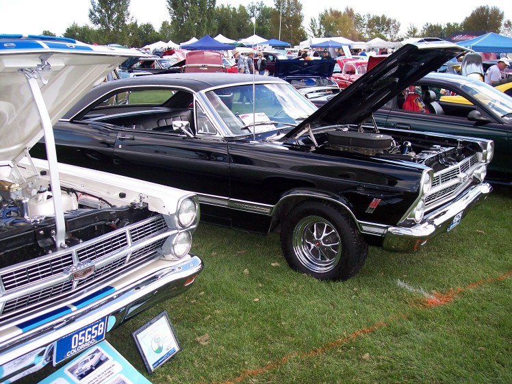 Black 1967 Ford Fairlane with hood open, parked next to a white car at a car show