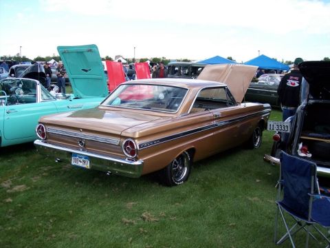 1972 Ford Ranchero - A gold 1964 Ford Falcon is parked on grass at an outdoor car show with its hood and trunk open.