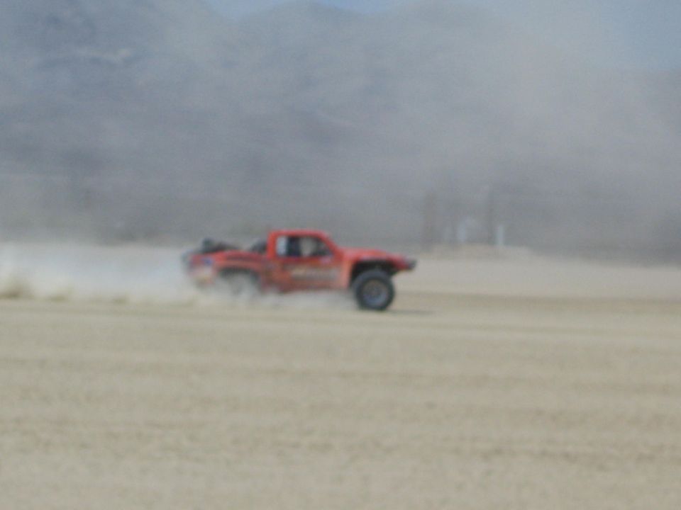 Orange off-road race truck speeding across dusty desert flat