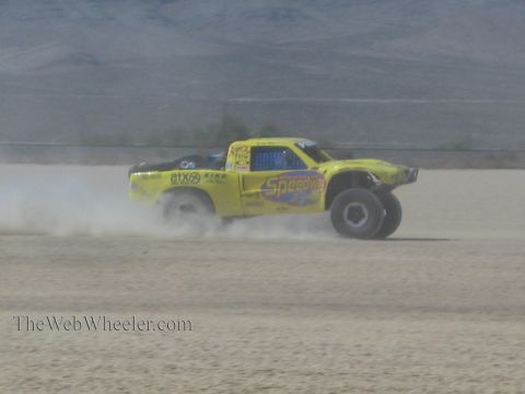 1990 Ford Bronco - yellow off-road race truck marked Speedco slides across a desert lakebed, throwing up dust as it races.