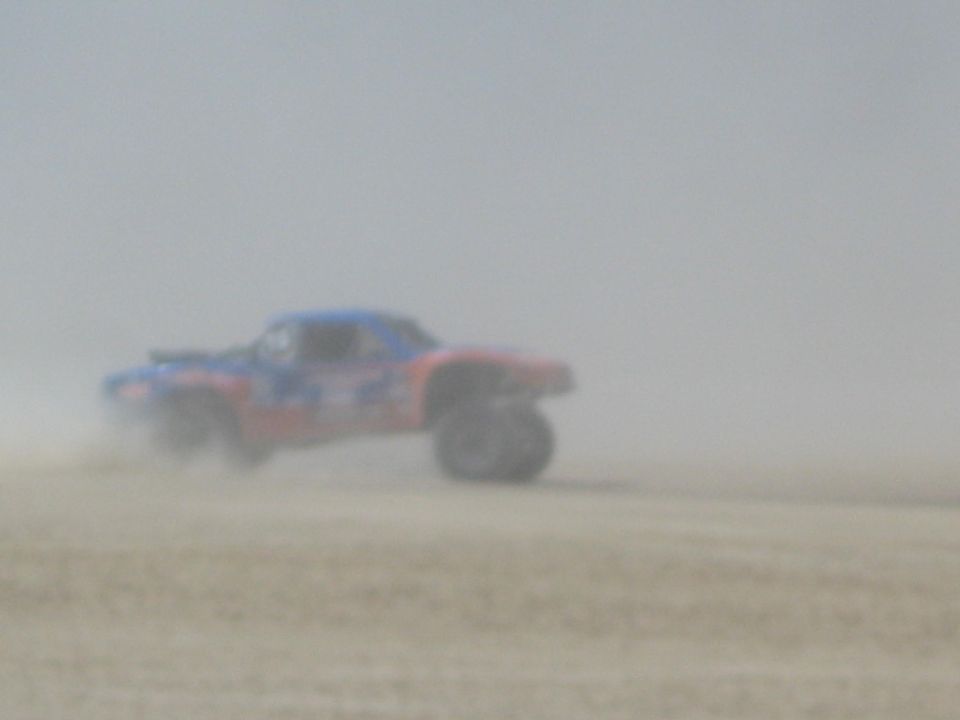 Red and blue off-road race truck in heavy dust on desert flat