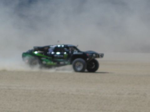 1990 Ford Bronco - black off-road race truck with green Monster graphics races across a dusty desert flat.