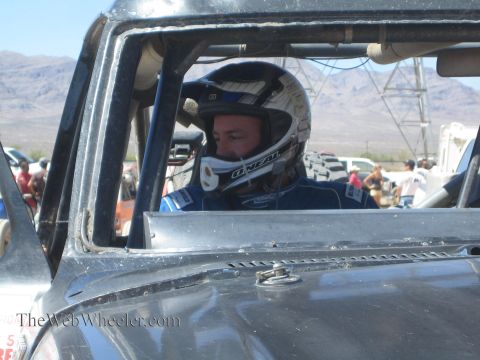 1990 Ford Bronco - driver wearing a white O'Neal helmet sits buckled into the roll-caged cockpit of an off-road race truck.