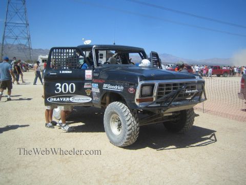 1990 Ford Bronco - black classic Ford pickup race truck numbered 300 with Deaver Suspension livery sits at a desert race under power lines.