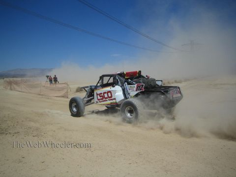 1990 Ford Bronco - white open-wheel off-road race buggy speeds through desert dust along a fenced course.