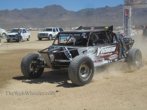 1990 Ford Bronco - black open-wheel off-road race buggy numbered 121 with Yochheim Racing livery races across a desert flat.