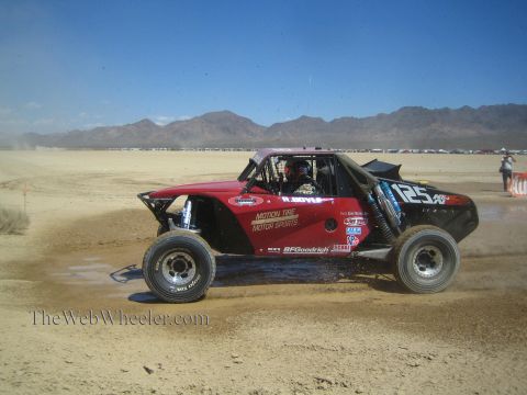 1990 Ford Bronco - dark red open-wheel off-road race buggy numbered 125 with Motion Tire livery races across a desert flat.
