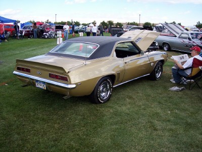 1972 Ford Ranchero - Gold 1969 Chevrolet Camaro SS with black vinyl top, hood open, parked on grass at car show.