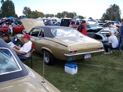 1972 Ford Ranchero - A gold coupe with a black vinyl top is displayed at an outdoor car show with other vehicles and attendees.