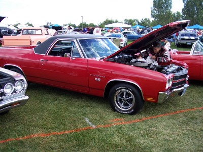 1972 Ford Ranchero - A person works on the engine of a red El Camino at an outdoor car show.