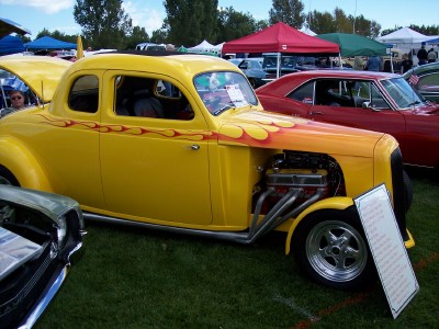 1972 Ford Ranchero - A custom yellow coupe with flame graphics and a visible engine is displayed at an outdoor car show, with other vehicles and tents in the ba…