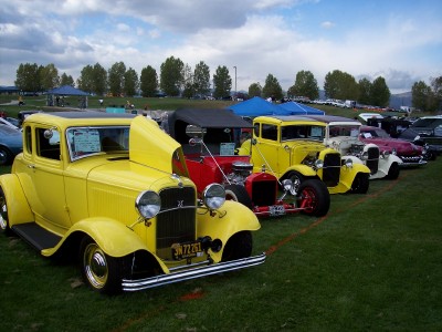 1972 Ford Ranchero - Several vintage hot rod vehicles are parked on a grassy field under a cloudy sky at an outdoor car show.
