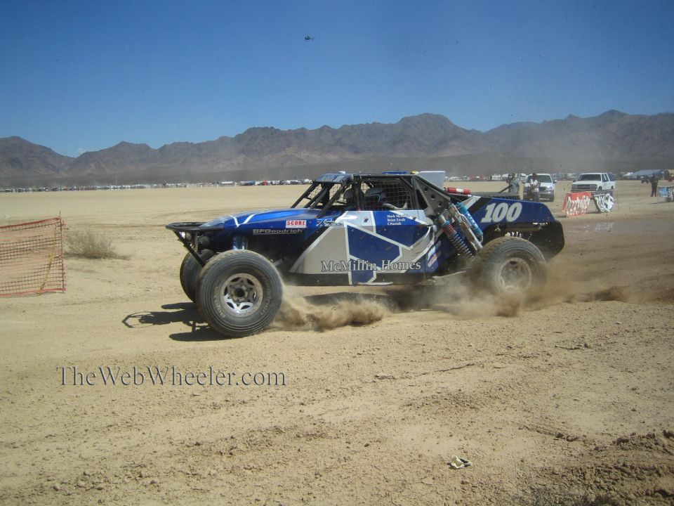 Blue and white off-road race buggy number 100 sliding through desert dirt