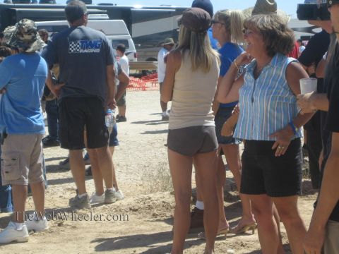 1990 Ford Bronco - group of casually dressed spectators stand and talk in a dusty pit area at a desert off-road racing event.