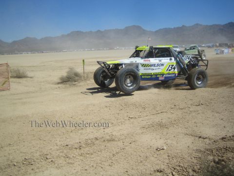 1990 Ford Bronco - white and yellow off-road race buggy numbered 134 with Wilson livery slides through dust on a desert race course.