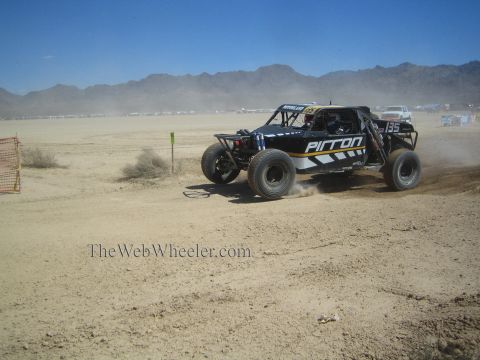 1990 Ford Bronco - black off-road race buggy numbered 135 with Pirron graphics races across a flat desert course under blue sky.