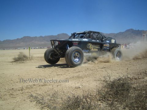 1990 Ford Bronco - black off-road race buggy numbered 137 with Corona Extra livery races across desert terrain trailing dust.