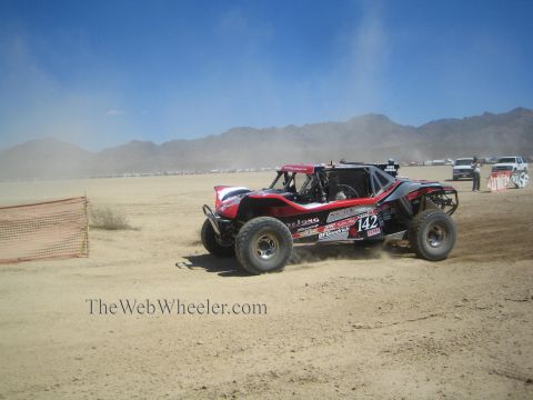 1990 Ford Bronco - red and black off-road race buggy numbered 142 corners through dust on a flat desert dry-lake course.