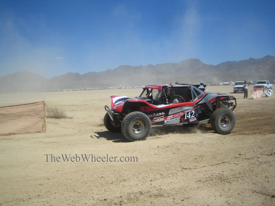 Red and black off-road race buggy number 142 cornering in desert dust