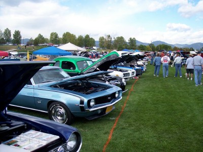 1972 Ford Ranchero - Outdoor car show features multiple classic vehicles lined up on a grassy field under a partly cloudy sky.