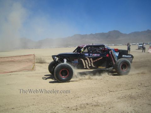 1990 Ford Bronco - black off-road race buggy numbered 144 with Monster-style graphics races a desert course trailing a dust cloud.