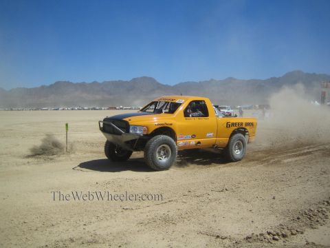 1990 Ford Bronco - yellow off-road race truck with Greer Bros livery races across a flat desert course kicking up dust.