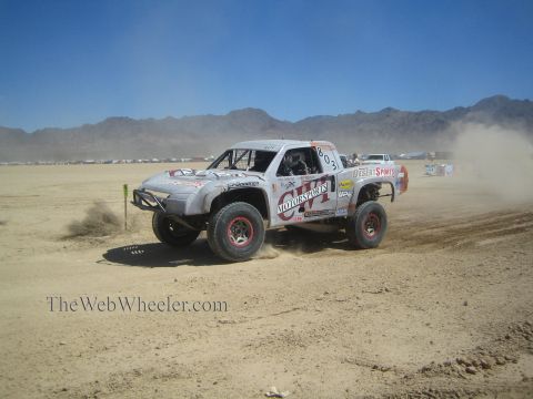 1990 Ford Bronco - silver off-road race truck numbered 803 with motorsports livery slides through dust on a desert course.