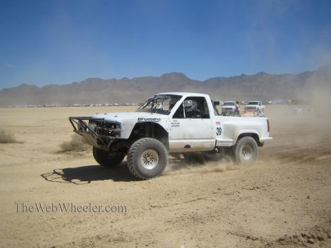 1990 Ford Bronco - white off-road race pickup numbered 39 with BFGoodrich decals races across a flat desert dry-lake course.