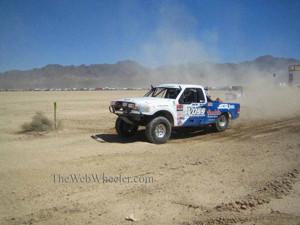White and blue off-road race pickup with Voss livery cornering in the desert