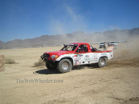 1990 Ford Bronco - red and white off-road race pickup with Yokohama livery slides through dust on a desert dry-lake course.