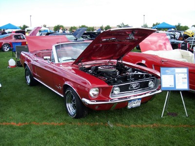 1972 Ford Ranchero - Red 1967 Ford Mustang convertible on display with hood open, other cars and a sign visible.