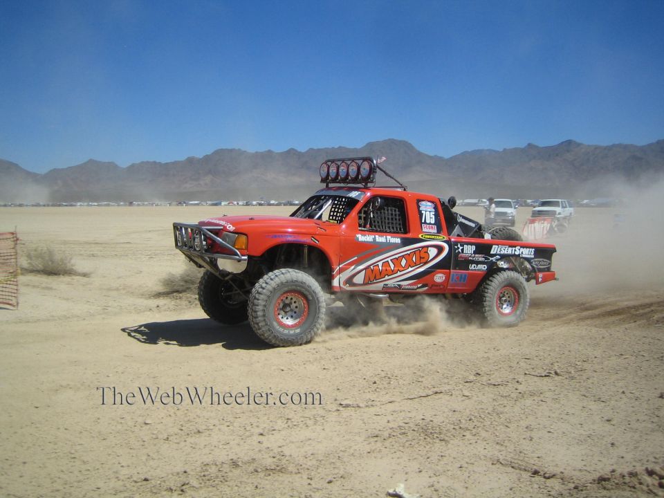 Orange Maxxis off-road race truck #785 racing through desert dust