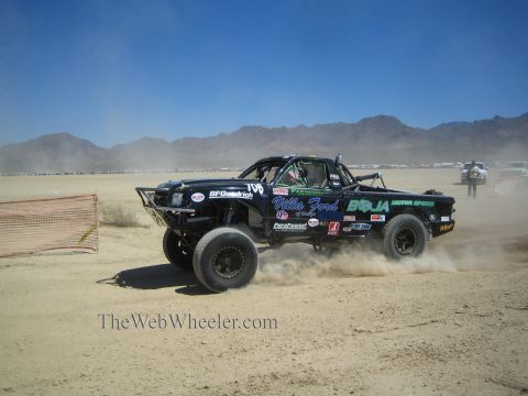 1990 Ford Bronco - black off-road race truck numbered 190 races across a dusty desert course with mountains in the background.